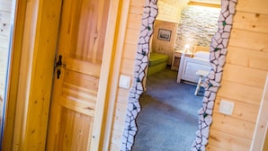 A wooden room with a stone wall, a bed, a bedside table, and a small stool. - Penzion Berc (Bled)