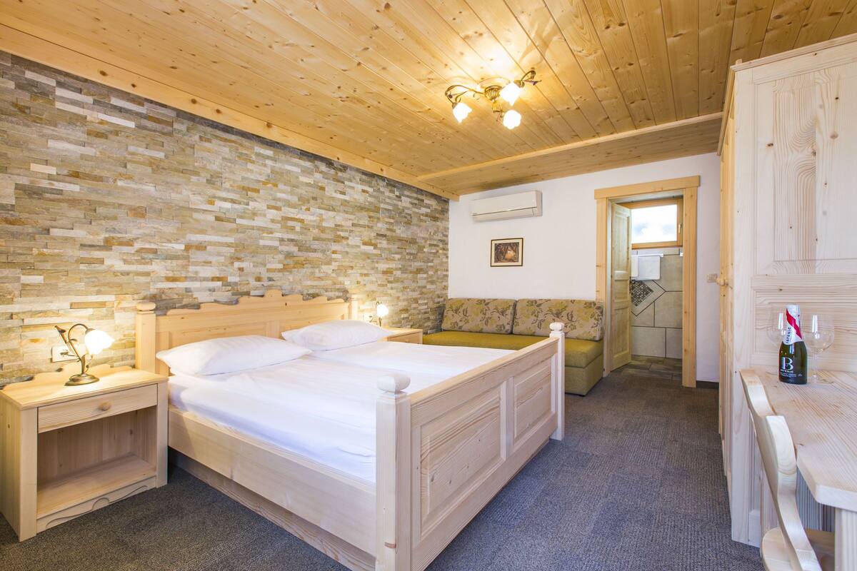 A wooden-paneled bedroom with a stone wall, a double bed, bedside tables, and a wooden bench.