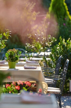 A table set outdoors with a green plant and folded napkins, surrounded by greenery.