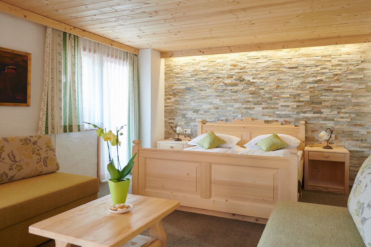 Ein gemütliches Zimmer mit einem hölzernen Bett, einer Zimmerpflanze, einem Nachttisch aus Holz und einer Steinwand.