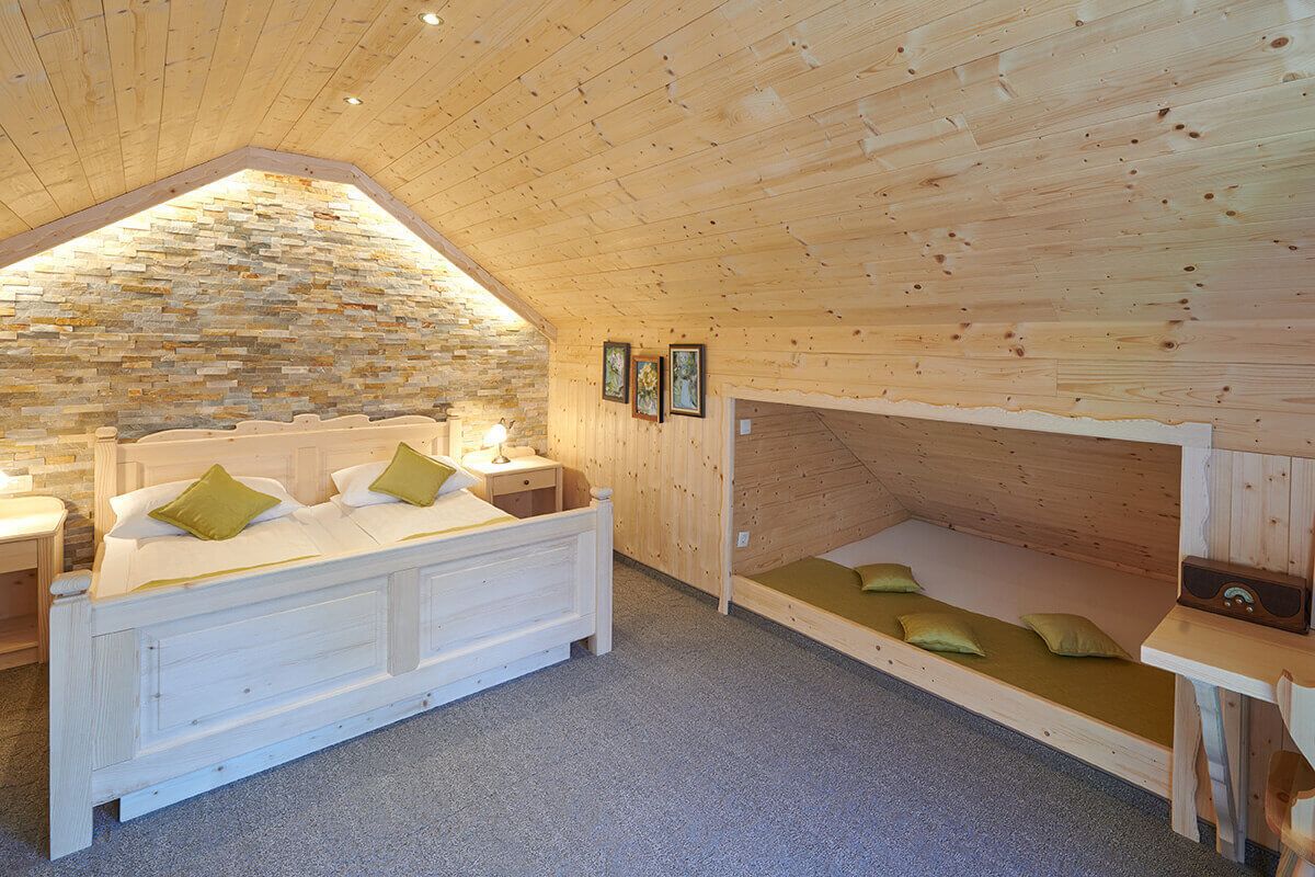 Un dormitorio acogedor con techo inclinado, pared de piedra, cama de madera, un banco con cojines y una radio.