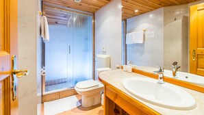 A modern bathroom with a wooden ceiling, a glass shower enclosure, a white toilet, and a large mirror above a sink.
