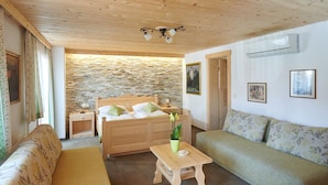 A cozy room with a wooden ceiling, a stone wall, a bed with green pillows, a wooden bench, a small table with a vase, and a green sofa. - Penzion Berc (Bled)