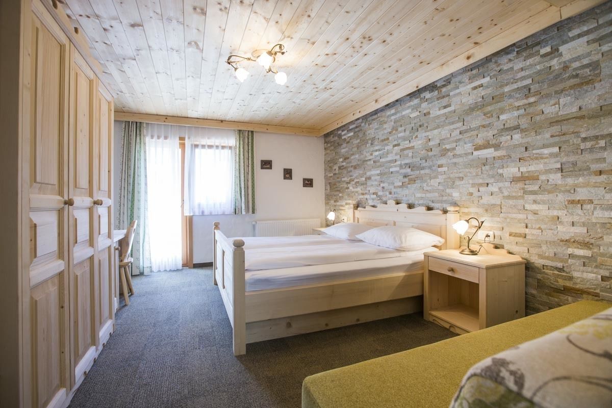 A bedroom with a wooden ceiling, a stone wall, a bed, a nightstand, and a chair.