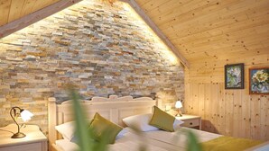 A bedroom with a stone wall, wooden ceiling, and a bed with pillows. - Penzion Berc (Bled)