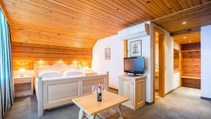 A cozy room with a wooden ceiling, a bed, a TV, and a small table with a bottle and glasses.