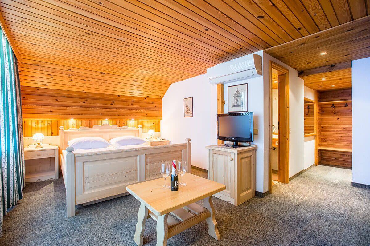 A cozy room with a wooden ceiling, a bed, a TV, and a small table with a bottle and glasses.