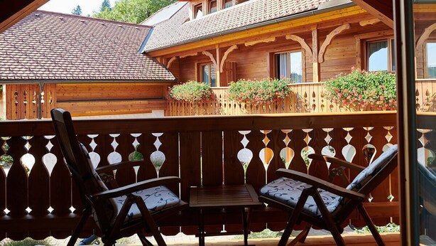 A wooden cabin with a balcony, two chairs, and a table.