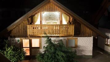 A wooden chalet with a balcony, a stone fireplace, and a small garden area.