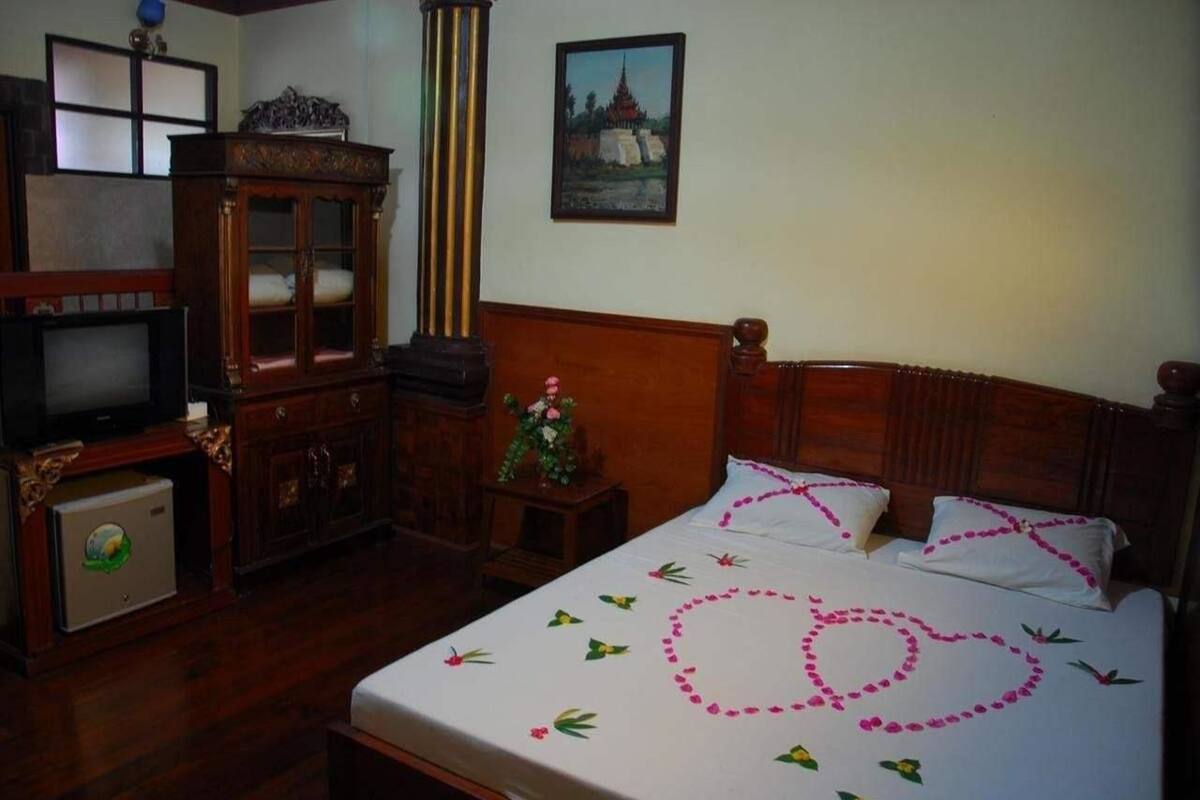 A hotel room with a wooden bed, a television, a cabinet, and a painting on the wall.