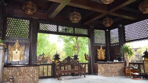 A traditional wooden structure with a stone wall, a bench, and decorative elements like a golden statue and lanterns. - Bagan Central Hotel (Nyaung-U)