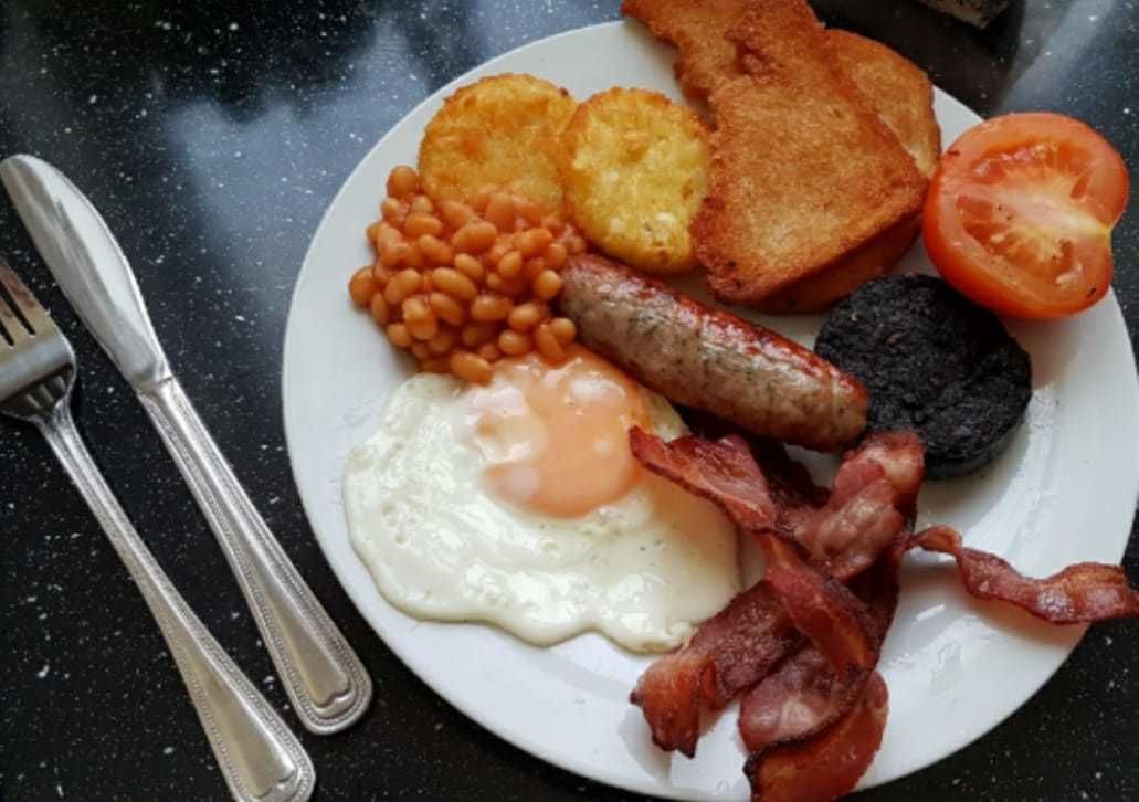 Ein Teller mit Frühstücksessen, darunter Eier, Speck, Würstchen, Toast, Bohnen und eine Tomate.