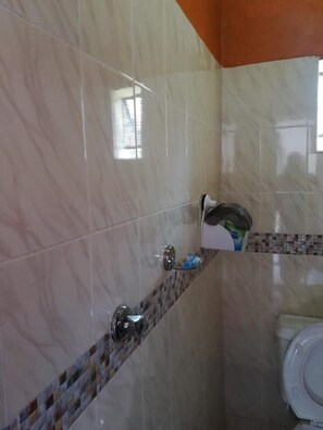 Un baño con azulejos de mármol, zona de ducha e inodoro.