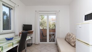 Ett kompakt rum med ett matbord, en soffa, en TV och en skjutdörr i glas som leder ut till ett utomhusområde.
