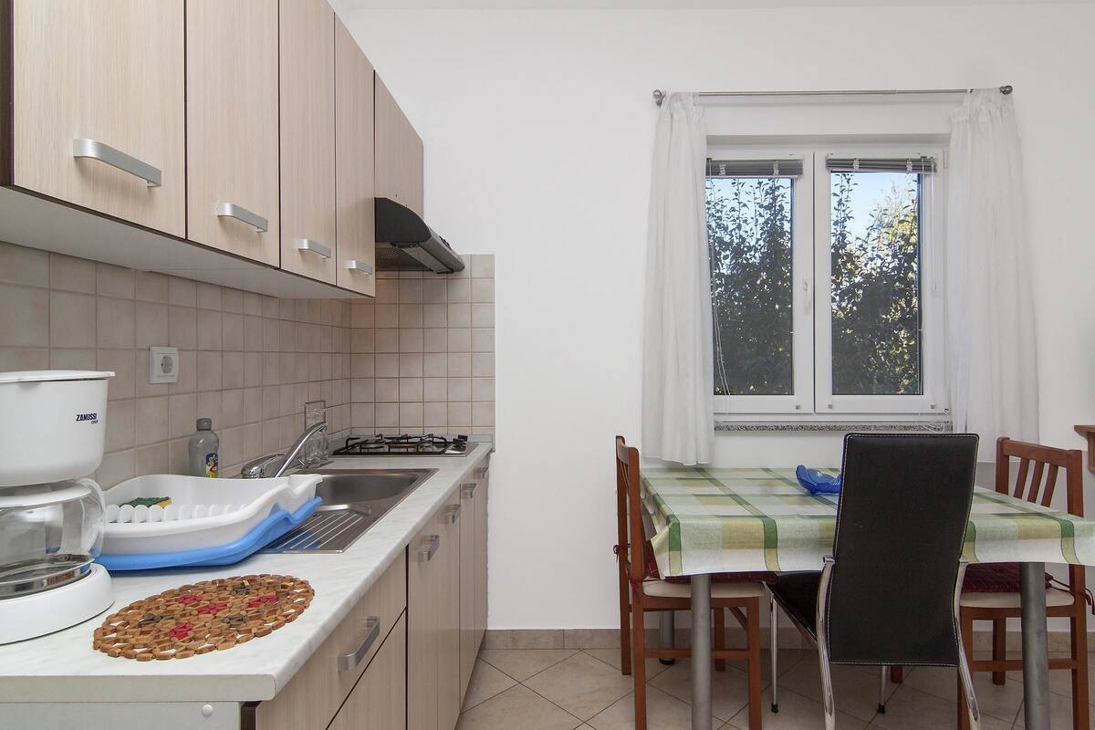 A kitchen with a dining area, a window with curtains, and a table with chairs.