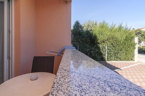 A balcony with a granite countertop, a chair, and a small table with a bowl. - Apartments Alen (Fazana)