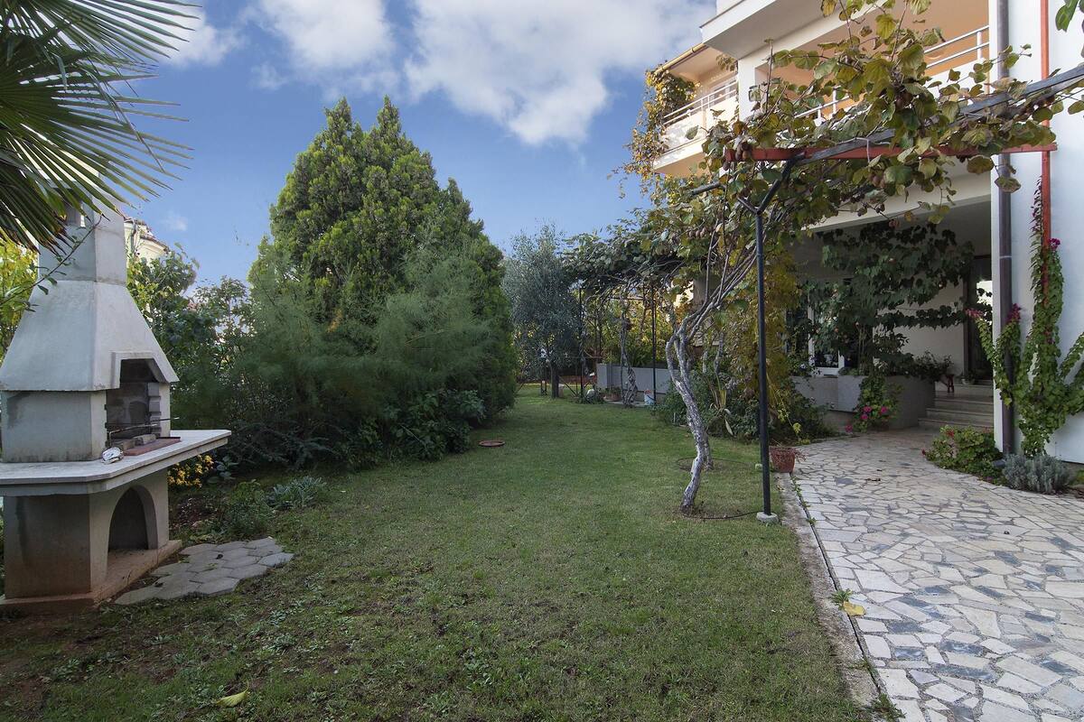 A garden with a barbecue area, a large tree, and a stone pathway leading to a building.