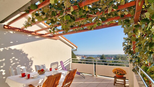 A balcony with a table set for two, a chair, a small stool, and a potted plant. - Apartments Levan Ceja (Medulin)