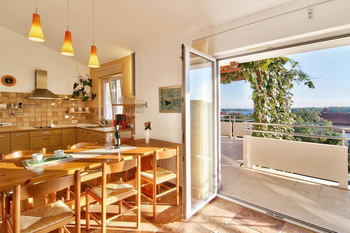 A modern kitchen with a large island, wooden chairs, and pendant lighting.
