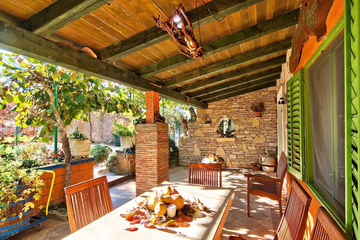 An outdoor patio with a stone wall, wooden furniture, and a table set for dining.