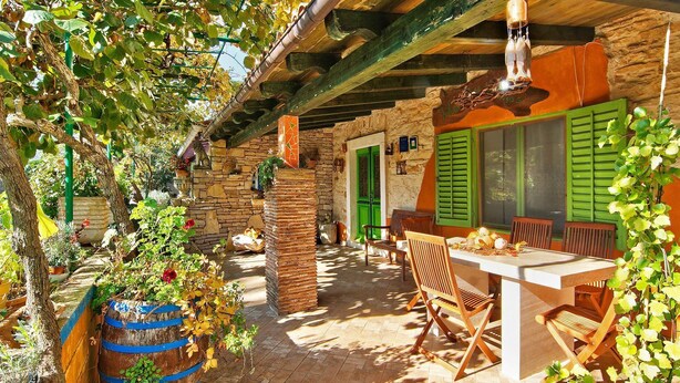 Un bâtiment rustique en pierre, doté d’un patio couvert, de meubles en bois et d’un luminaire suspendu.