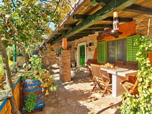 Un bâtiment rustique en pierre, doté d’un patio couvert, de meubles en bois et d’un luminaire suspendu.