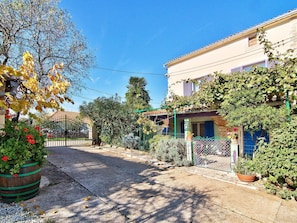 Une rue tranquille avec une maison dotée d’un balcon, un jardin agrémenté de plantes en pot et un ciel d’un bleu limpide.