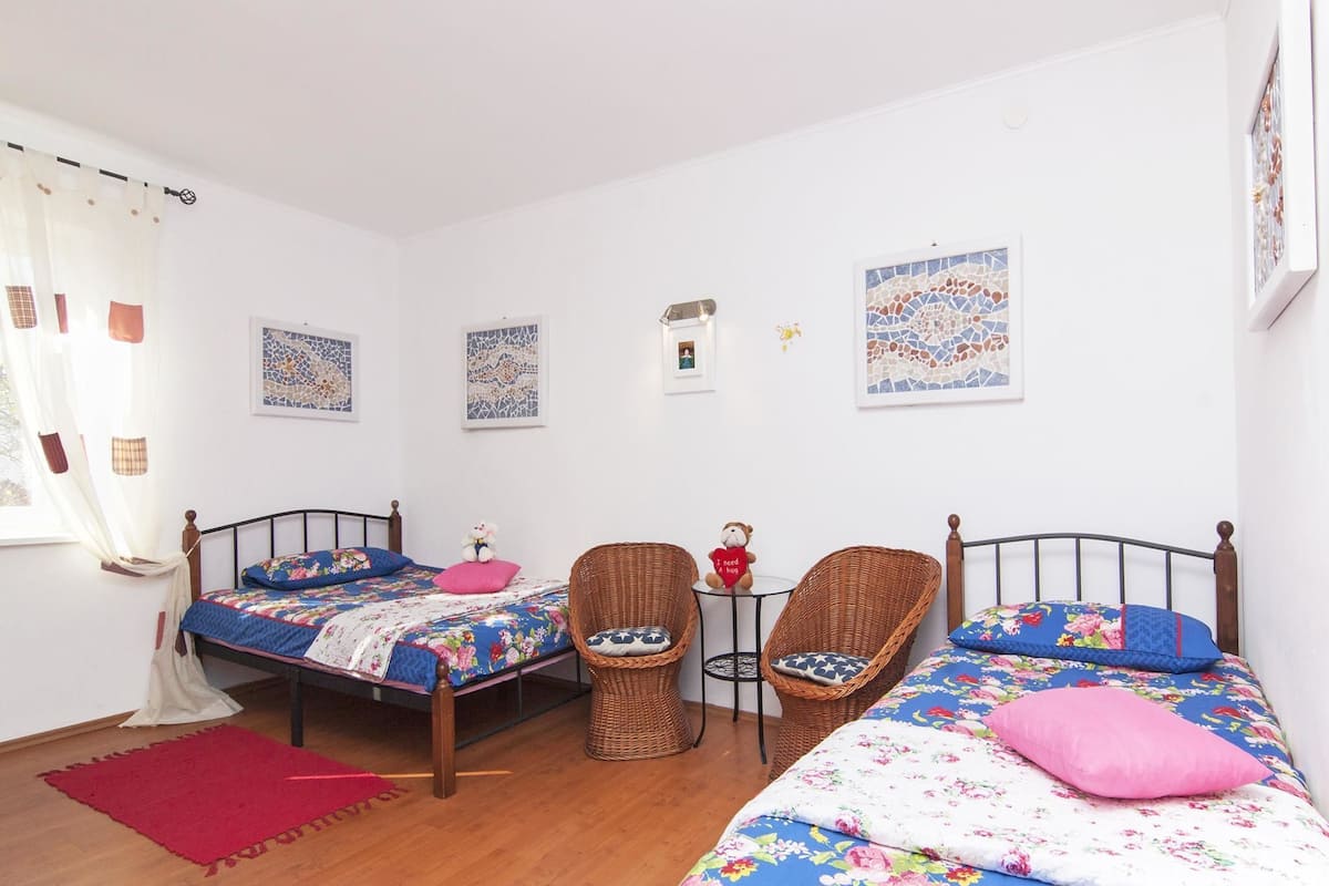 A bedroom with two beds, wicker chairs, a small table, and wall art.