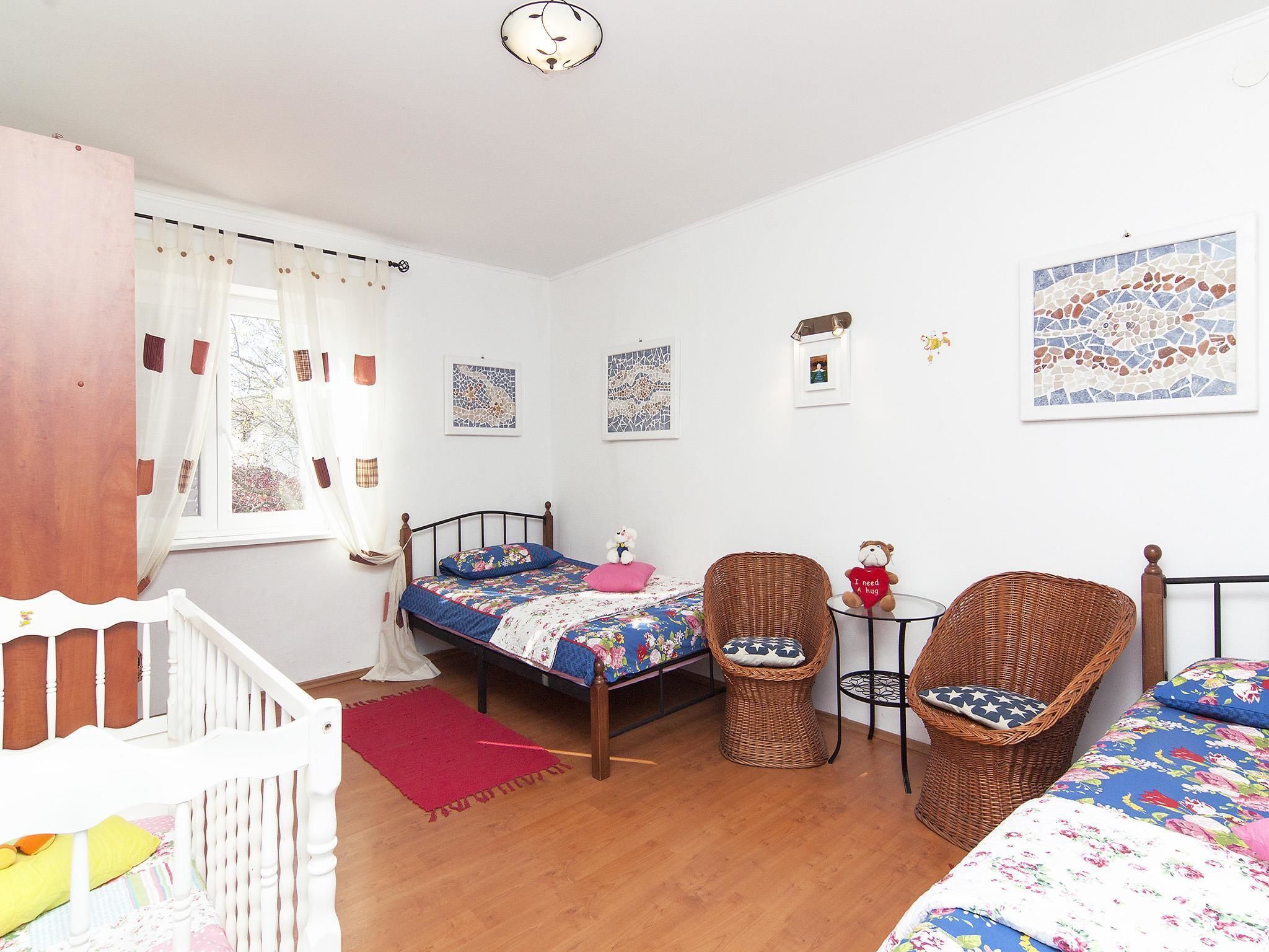 Ein Schlafzimmer mit einem Bett, zwei Korbstühlen, einem kleinen Tisch und einem Babybett.