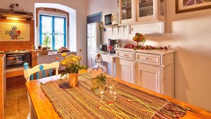 Une cuisine chaleureuse avec une table en bois dressée pour le repas, un four encastré et une fenêtre avec des volets bleus.