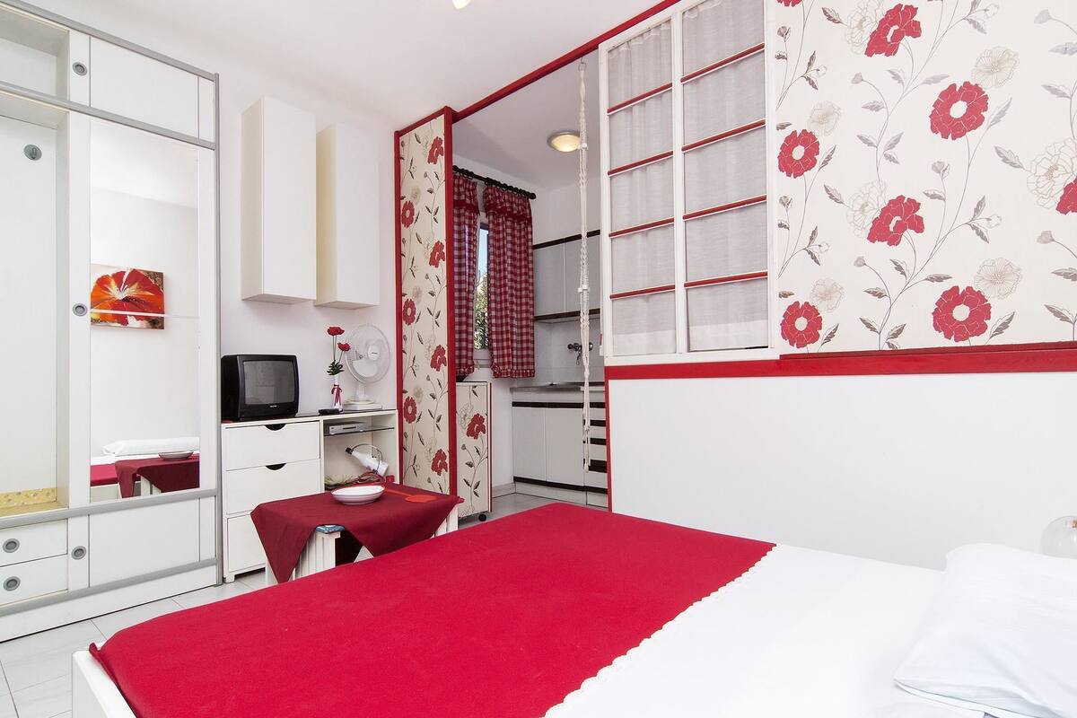 A bedroom with a bed, a desk, a mirror, and a wardrobe.