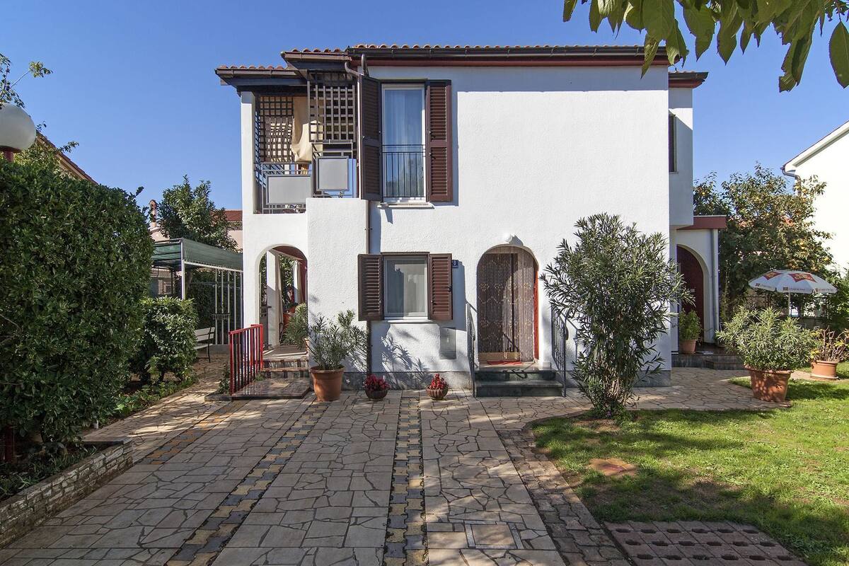 A two-story house with a stone-paved courtyard, a balcony, and a small garden area.