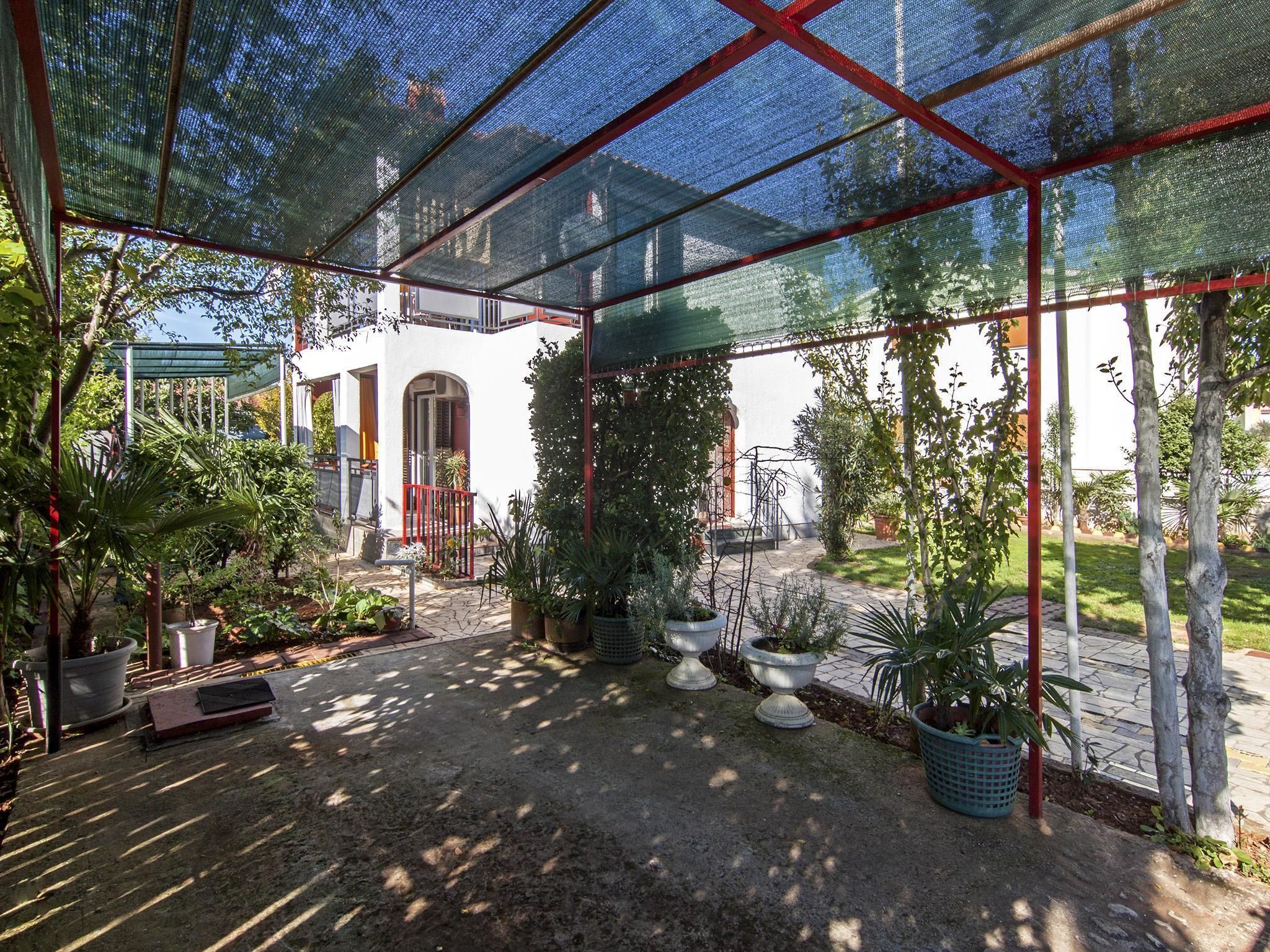 Un'area esterna riparata con piante in vaso e un vialetto che conduce a un edificio bianco con una porta rossa.