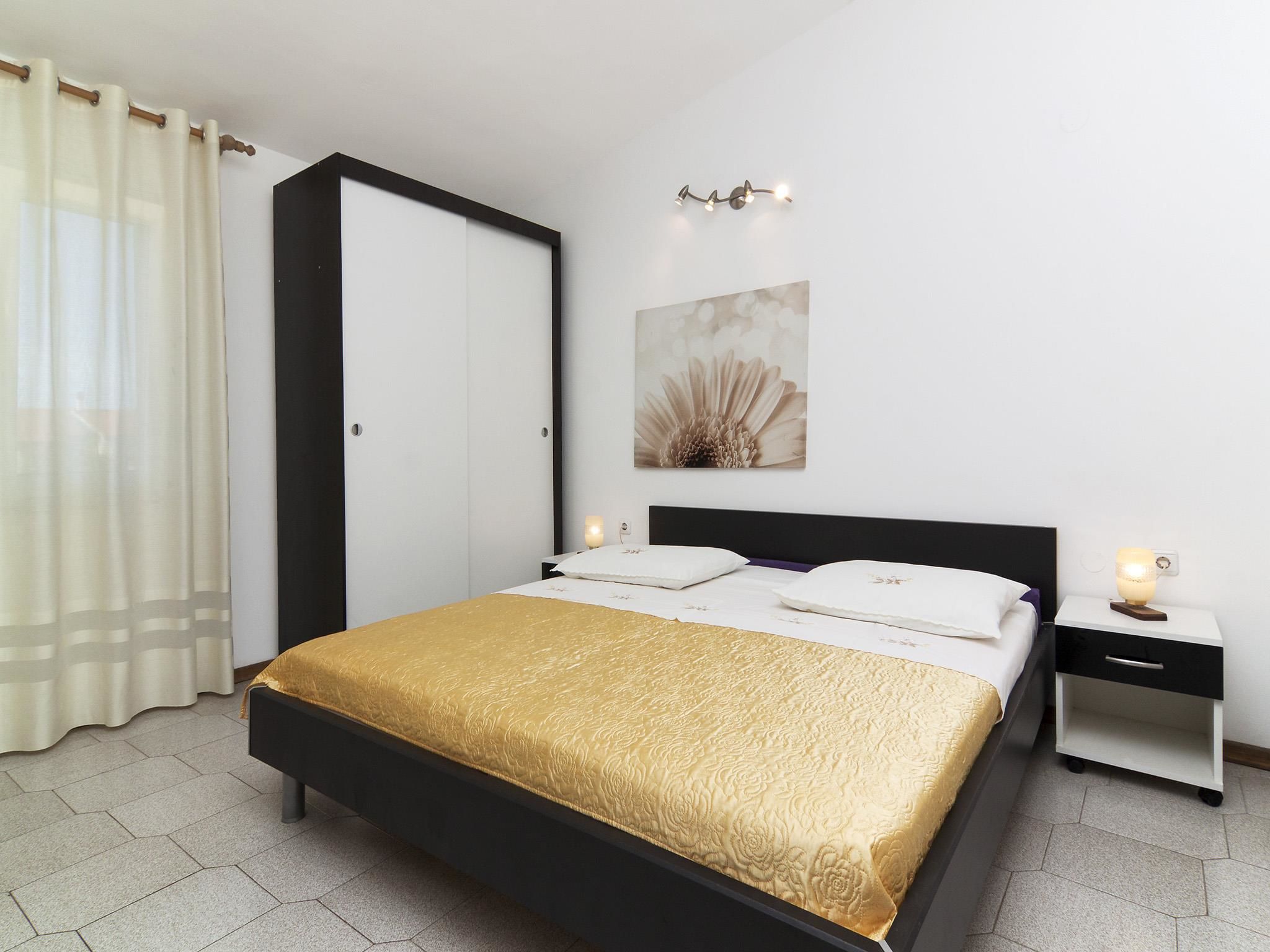 Une chambre à coucher comprenant un lit, une table de chevet, une commode, une armoire et un luminaire fixé au mur.