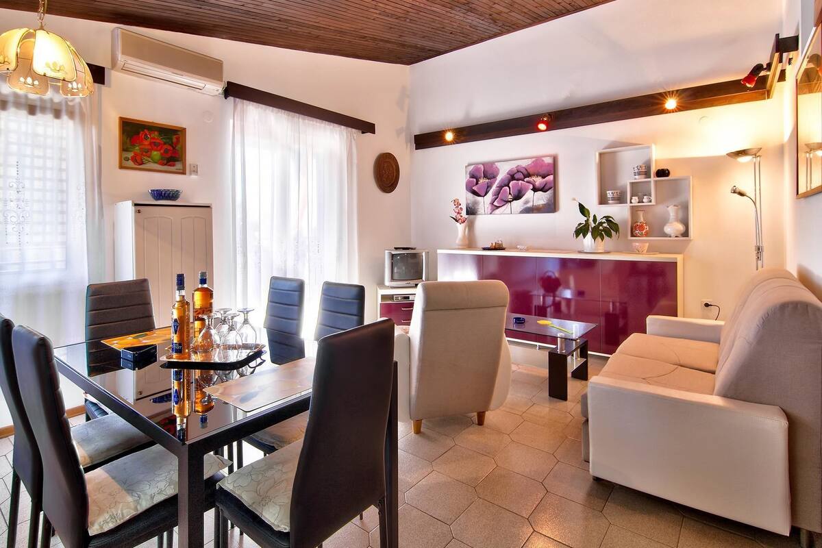 A modern living room with a dining area, featuring a wooden ceiling, a TV, and a sofa.