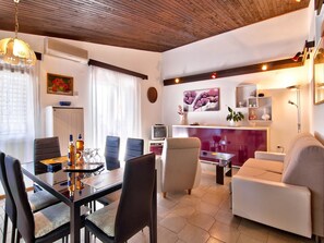 A modern living room with a dining area, featuring a wooden ceiling, a TV, and a sofa. - Apartments Ana Valbandon (Fazana)