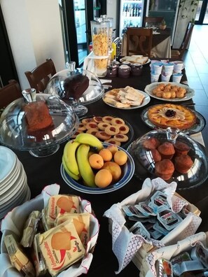 A buffet table with various food items including fruits, pastries, and packaged goods. - Ostello Ortensi (Farnese)