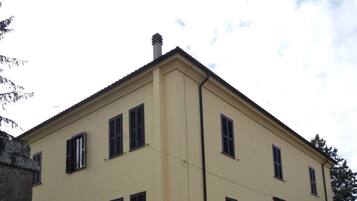 Ein zweistöckiges Gebäude mit gelber Fassade, zahlreichen Fenstern und einer Steintreppe, die zu einem verschlossenen Eingang führt.