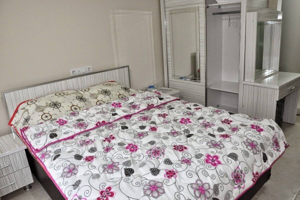 A bedroom with a bed, a bedside table, a mirror, and a wardrobe.