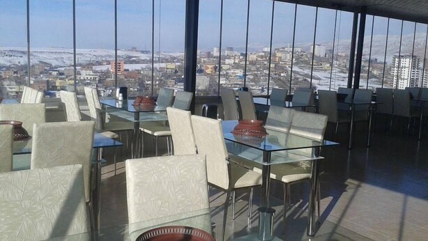 A restaurant with glass tables and chairs, offering a city view through large windows. - Grand Silvan Otel (Silvan)