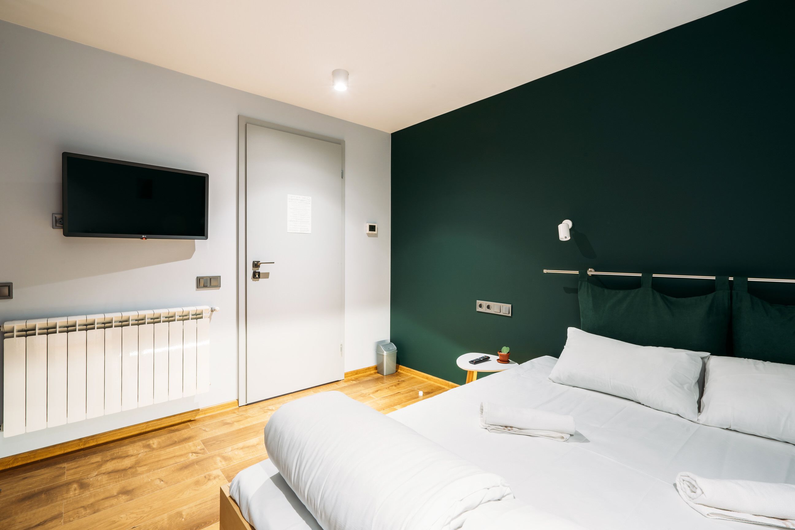 Een moderne hotelkamer met een groot bed, een flatscreen televisie aan de muur, een nachtkastje met een afstandsbediening en een radiator.