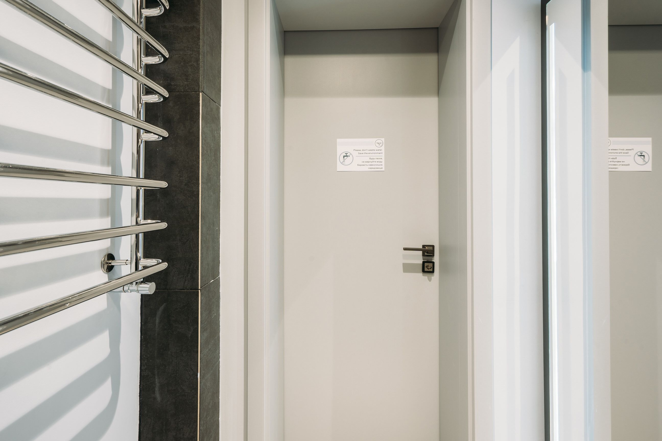 A modern bathroom with a glass shower enclosure, a towel rack, and a door with a lock.