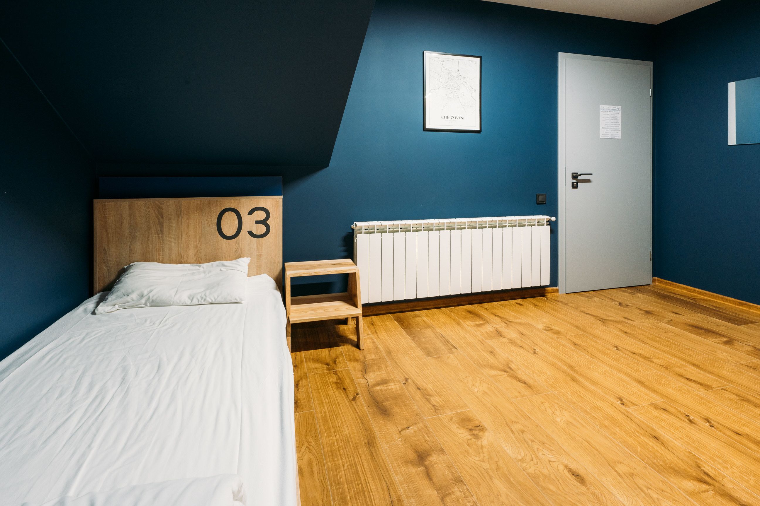 A bedroom with a bed, a wooden headboard with the number 03, a white radiator, and a door with a notice on it.