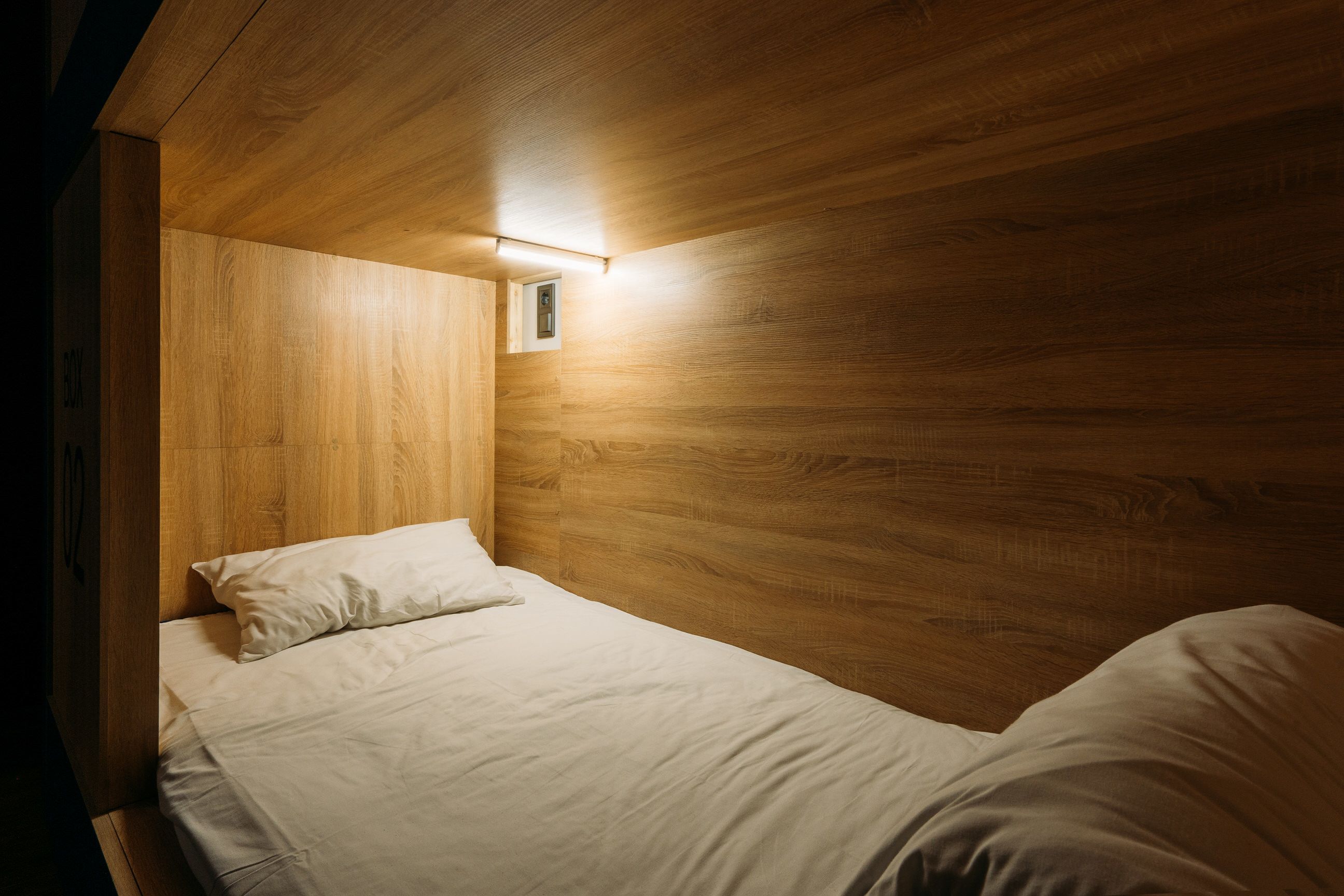 Ein Einzelbett mit Holz-Kopfteil und einem kleinen Fenster.