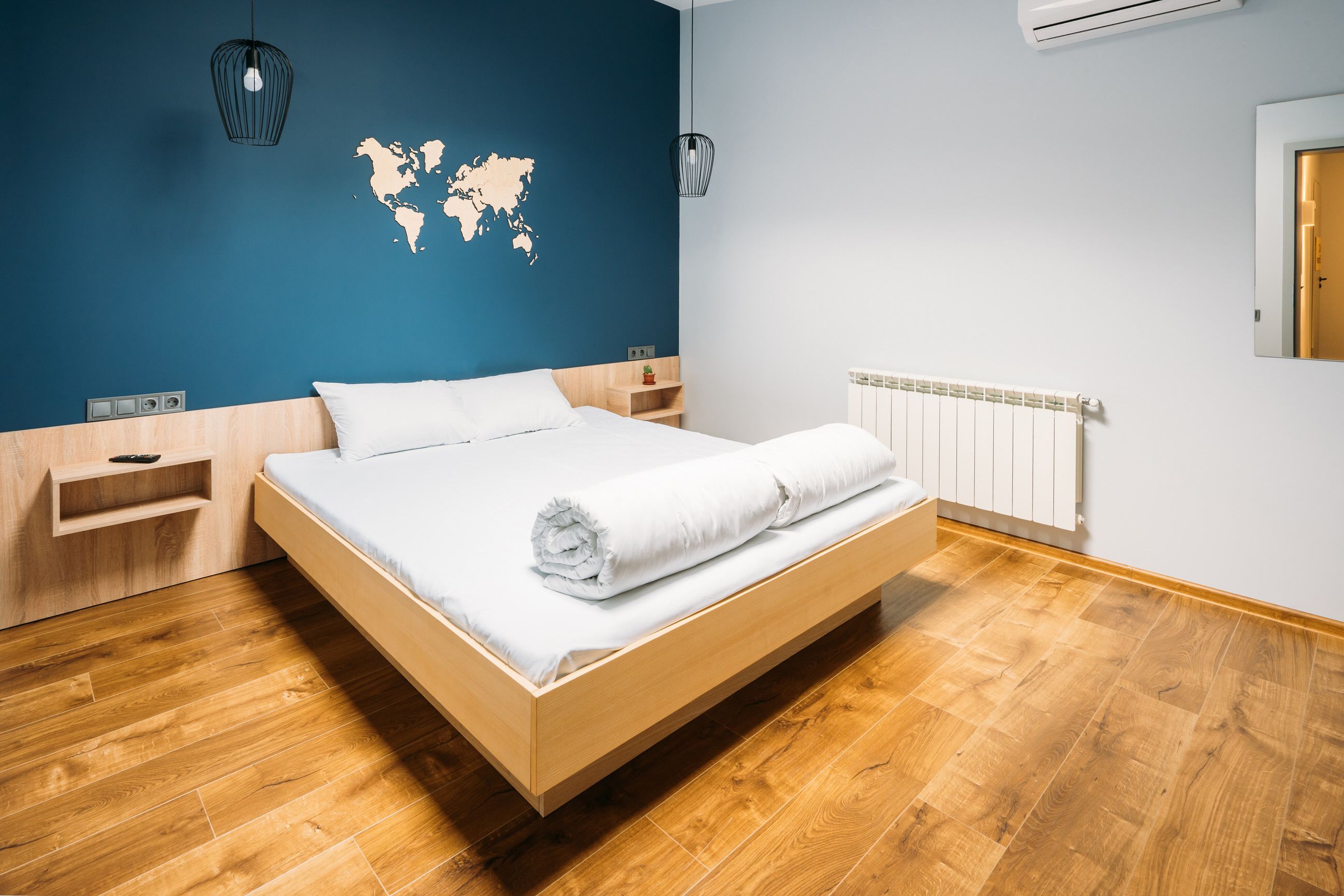 A modern bedroom with a wooden bed, a world map on the wall, and a wooden floor.