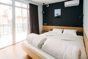 A hotel room with a large bed, a bedside table, an air conditioning unit, a wall-mounted picture, and a view through a sliding glass door. - Yard Hostel & Coffee (Chernivtsi)