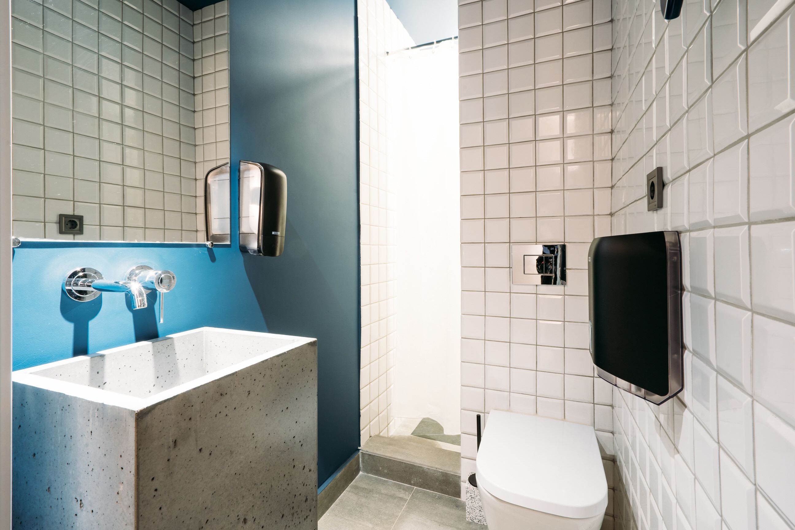 Un baño con una pared azul decorativa, un lavamanos blanco, un inodoro y un secamanos.