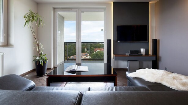 A modern living room with a sofa, a coffee table, a TV, and a balcony with a view of the city. - ELITE APARTMENTS Tre Mare Residence (Gdansk)