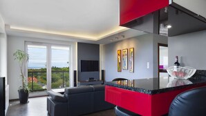 A modern living room with a large window, a grey sofa, a red accent wall, and a flat-screen TV. - ELITE APARTMENTS Tre Mare Residence (Gdansk)