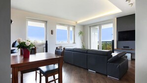 A modern living room with a wooden dining table, a grey sofa, and a TV mounted on the wall. - ELITE APARTMENTS Tre Mare Residence (Gdansk)